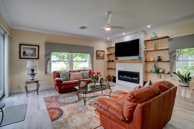 living room featuring light wood-type flooring, ceiling fan, a fireplace, ornamental molding, and a textured ceiling