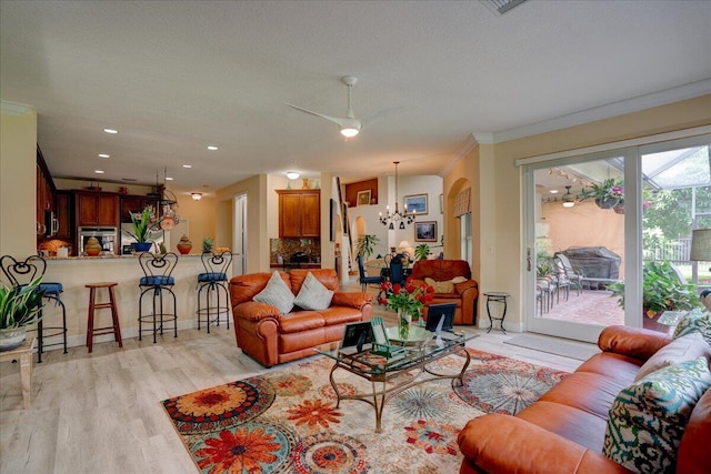 living room with ceiling fan with notable chandelier, light wood-type flooring, and crown molding