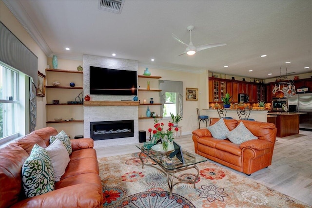 living room featuring ornamental molding, light wood-type flooring, a fireplace, and ceiling fan