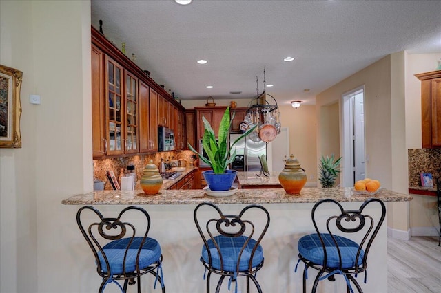 kitchen with light hardwood / wood-style floors, kitchen peninsula, appliances with stainless steel finishes, light stone countertops, and a kitchen bar