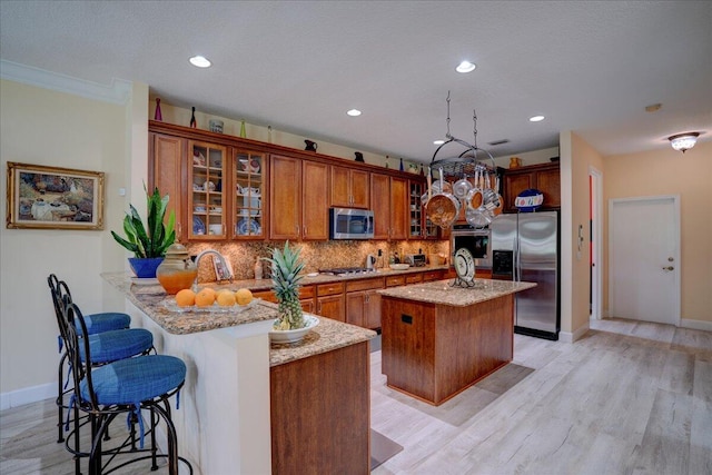 kitchen with light hardwood / wood-style floors, a center island with sink, light stone countertops, stainless steel appliances, and kitchen peninsula