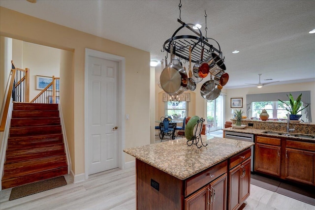 kitchen with light wood-type flooring, light stone counters, a center island, sink, and a textured ceiling