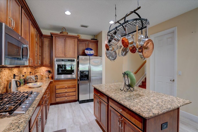 kitchen featuring tasteful backsplash, a kitchen island, light hardwood / wood-style flooring, stainless steel appliances, and light stone countertops