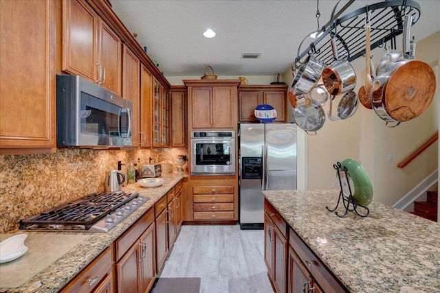 kitchen with light wood-type flooring, light stone counters, decorative backsplash, stainless steel appliances, and a textured ceiling