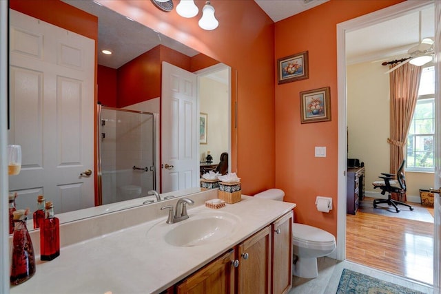 bathroom with ceiling fan, vanity, wood-type flooring, an enclosed shower, and toilet