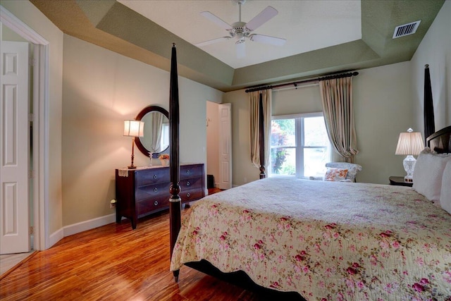 bedroom with ceiling fan, a raised ceiling, and hardwood / wood-style floors