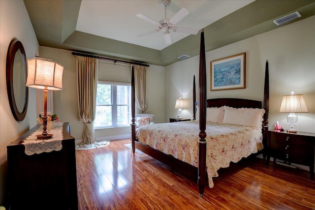 bedroom featuring ceiling fan, a tray ceiling, and wood-type flooring