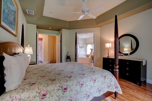 bedroom featuring a tray ceiling, hardwood / wood-style floors, ensuite bath, and ceiling fan