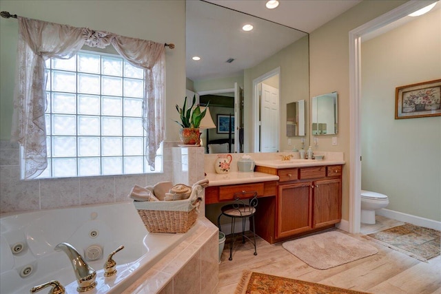 bathroom featuring hardwood / wood-style flooring, a relaxing tiled tub, vanity, and toilet