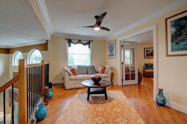 living room with ornamental molding, light wood-type flooring, ceiling fan, and a textured ceiling