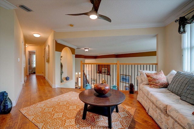 living room with crown molding, light hardwood / wood-style flooring, a textured ceiling, and ceiling fan