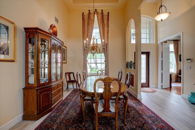 dining area with a high ceiling, light wood-type flooring, and an inviting chandelier