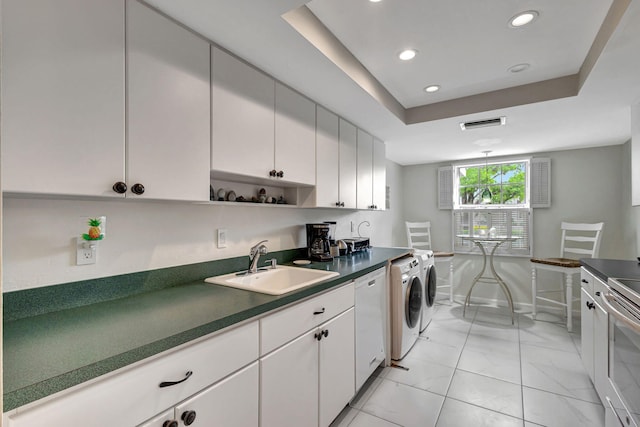 kitchen with white cabinets, a raised ceiling, white dishwasher, washing machine and dryer, and sink