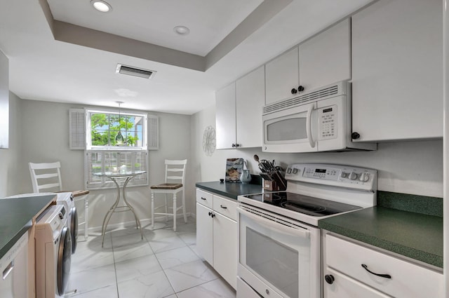 kitchen with white appliances, washer / dryer, and white cabinets