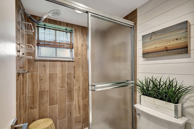 bathroom with toilet, a shower with shower door, and wooden walls