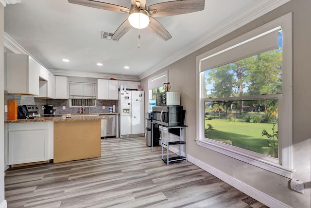 kitchen with light stone counters, white cabinets, crown molding, light wood-type flooring, and appliances with stainless steel finishes