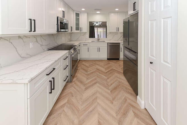 kitchen with white cabinets, light parquet flooring, backsplash, appliances with stainless steel finishes, and light stone countertops