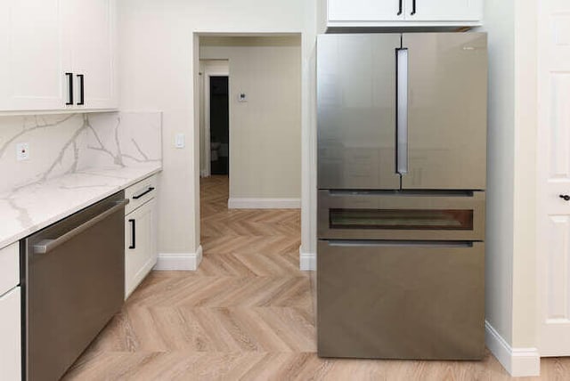 kitchen featuring light stone counters, tasteful backsplash, light parquet flooring, white cabinetry, and appliances with stainless steel finishes