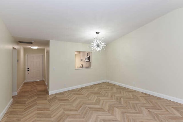 empty room with light parquet flooring and an inviting chandelier