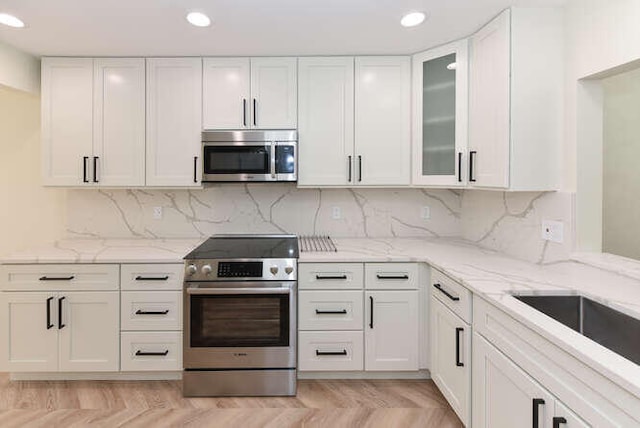 kitchen with decorative backsplash, appliances with stainless steel finishes, light stone counters, and white cabinetry