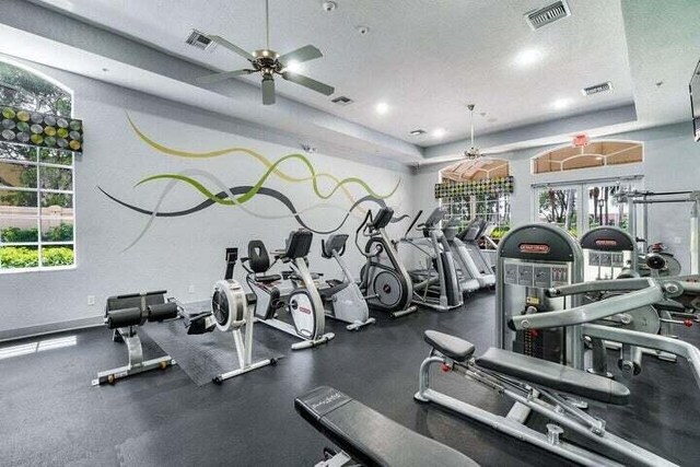 gym featuring a textured ceiling, ceiling fan, a tray ceiling, and a wealth of natural light