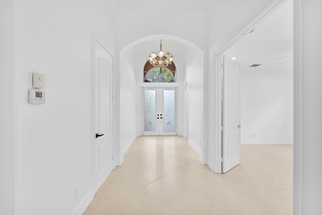 hall with a chandelier, crown molding, french doors, and light tile patterned floors