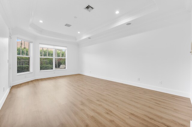 empty room featuring light hardwood / wood-style flooring, ornamental molding, and a raised ceiling