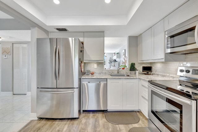 kitchen featuring appliances with stainless steel finishes, sink, white cabinetry, light stone counters, and decorative backsplash