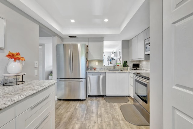 kitchen with decorative backsplash, sink, light wood-type flooring, white cabinetry, and appliances with stainless steel finishes