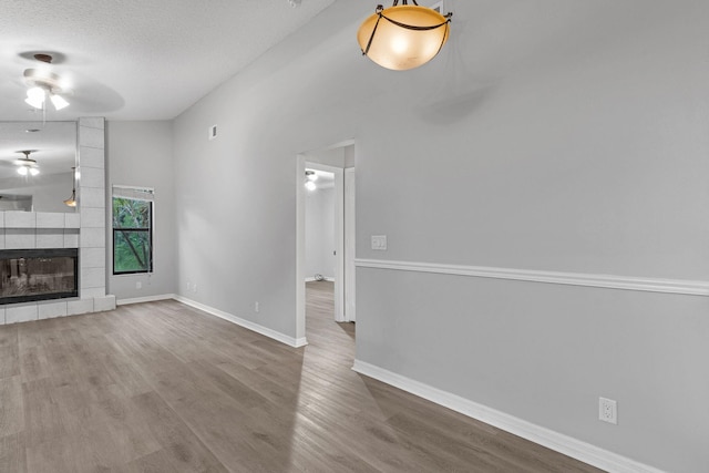 unfurnished living room with a large fireplace, wood-type flooring, a textured ceiling, and ceiling fan