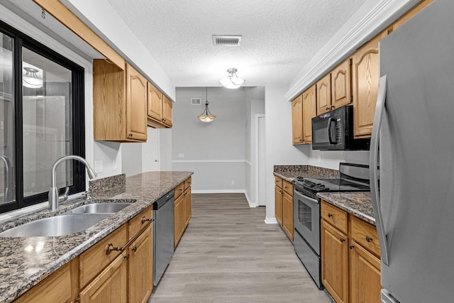 kitchen featuring light hardwood / wood-style flooring, dark stone countertops, sink, stainless steel appliances, and a textured ceiling