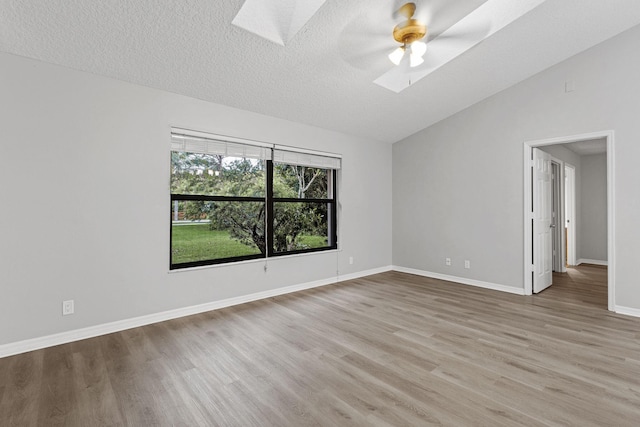 unfurnished room featuring vaulted ceiling with skylight, light hardwood / wood-style flooring, a textured ceiling, and ceiling fan