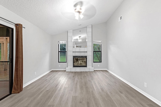 unfurnished living room with lofted ceiling, ceiling fan, hardwood / wood-style flooring, a fireplace, and a textured ceiling