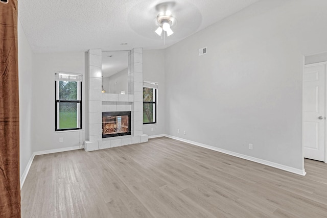 unfurnished living room featuring a tiled fireplace, a wealth of natural light, and light hardwood / wood-style flooring