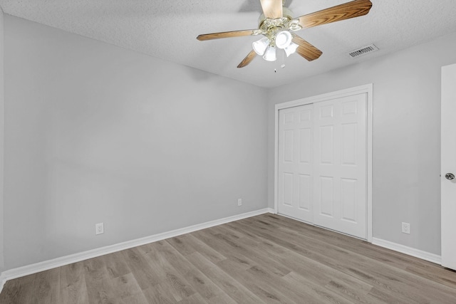 unfurnished bedroom featuring a textured ceiling, a closet, light wood-type flooring, and ceiling fan