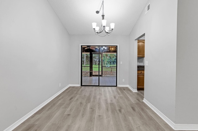 unfurnished dining area featuring light hardwood / wood-style floors, vaulted ceiling, a chandelier, and a textured ceiling