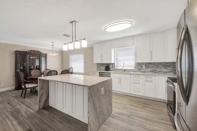 kitchen featuring a kitchen island, white cabinetry, decorative light fixtures, and stainless steel appliances