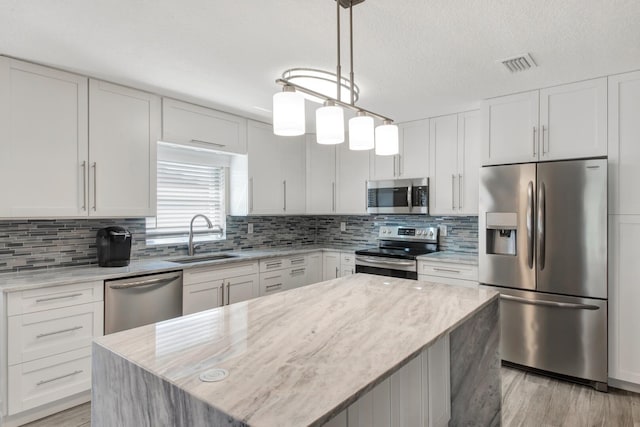 kitchen featuring white cabinetry, appliances with stainless steel finishes, decorative light fixtures, and a kitchen island