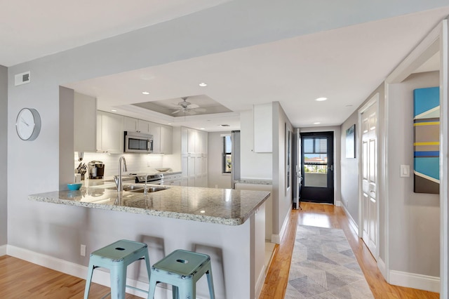 kitchen with white cabinets, a raised ceiling, sink, light stone countertops, and kitchen peninsula