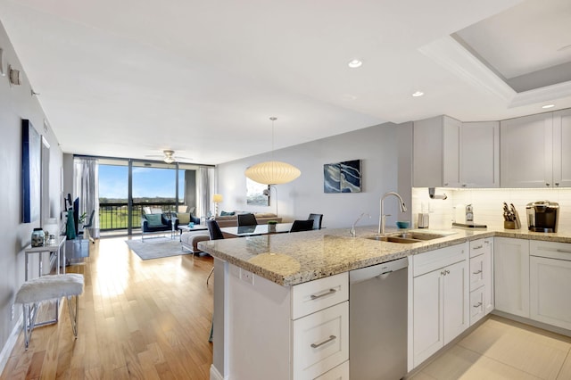 kitchen featuring white cabinetry, sink, expansive windows, stainless steel dishwasher, and light stone countertops