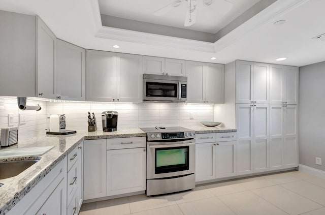 kitchen with appliances with stainless steel finishes, light stone countertops, light tile patterned flooring, decorative backsplash, and a raised ceiling