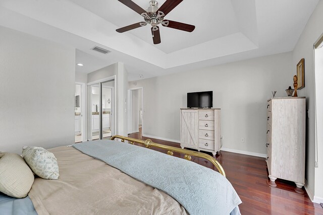 bedroom with ceiling fan, a raised ceiling, dark hardwood / wood-style flooring, ensuite bathroom, and a closet