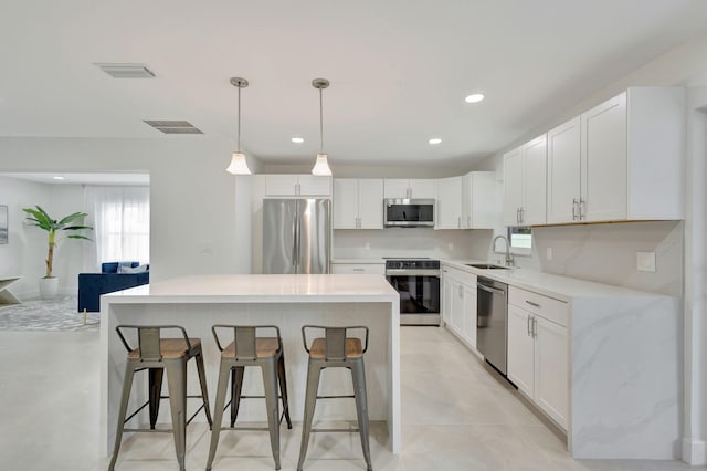 kitchen with white cabinets, appliances with stainless steel finishes, sink, pendant lighting, and a center island