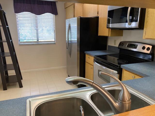 2811 Village Blvd Unit 106, West Palm Beach, FL 33409 - kitchen with stainless steel appliances, a sink, light brown cabinets, and baseboards