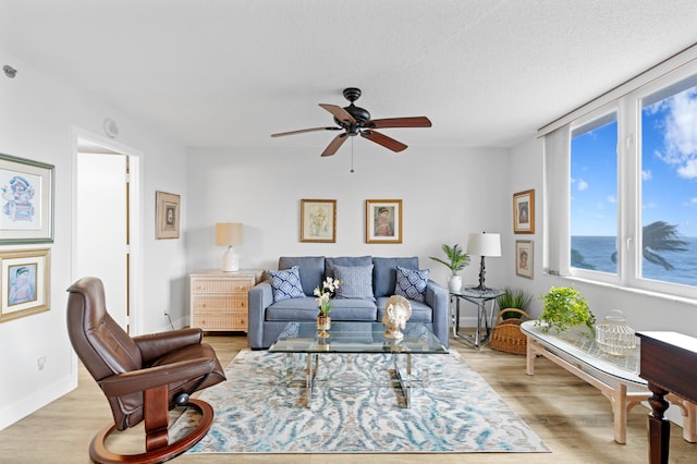 living room featuring light hardwood / wood-style flooring, a textured ceiling, a water view, and ceiling fan