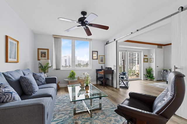 living room with light hardwood / wood-style flooring, a barn door, a healthy amount of sunlight, and ceiling fan