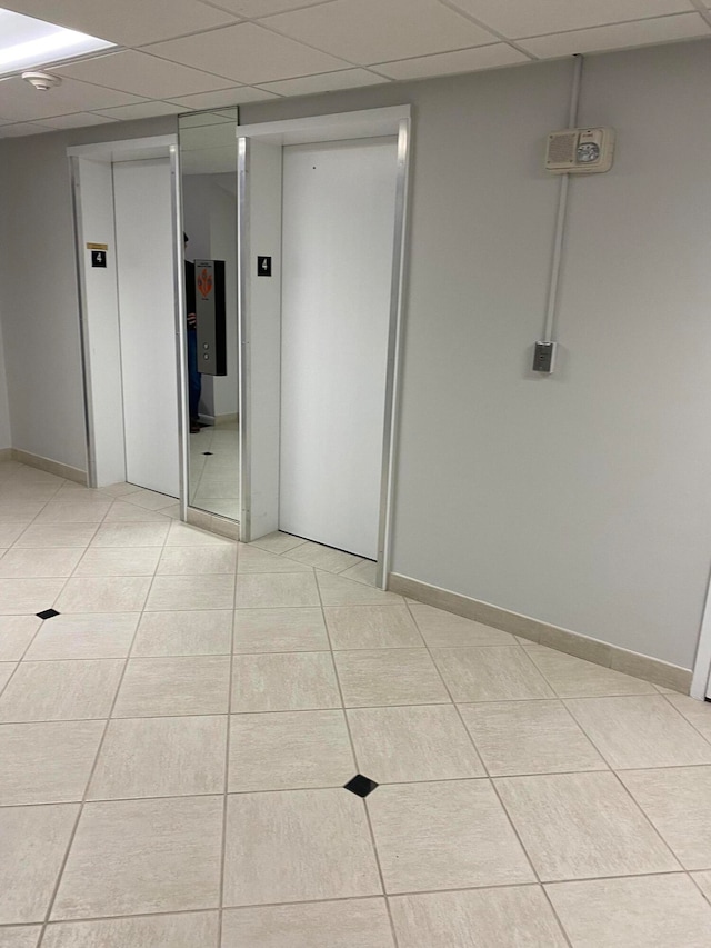 interior space with elevator, a paneled ceiling, and light tile patterned floors