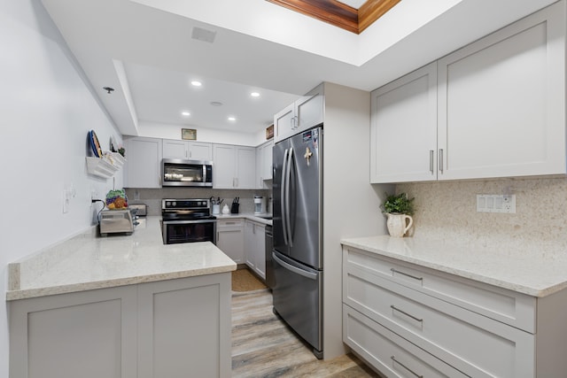 kitchen featuring light stone countertops, light hardwood / wood-style floors, appliances with stainless steel finishes, and backsplash