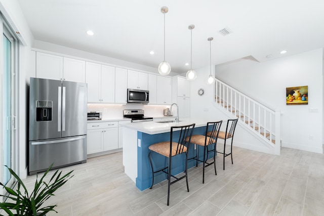 kitchen featuring light hardwood / wood-style flooring, hanging light fixtures, a center island with sink, white cabinetry, and appliances with stainless steel finishes