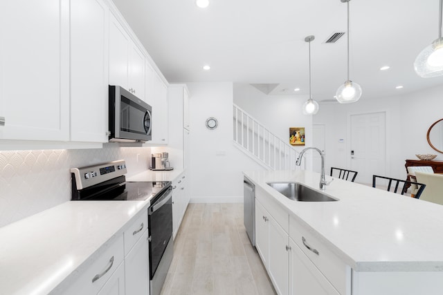 kitchen featuring hanging light fixtures, white cabinetry, a kitchen island with sink, sink, and stainless steel appliances